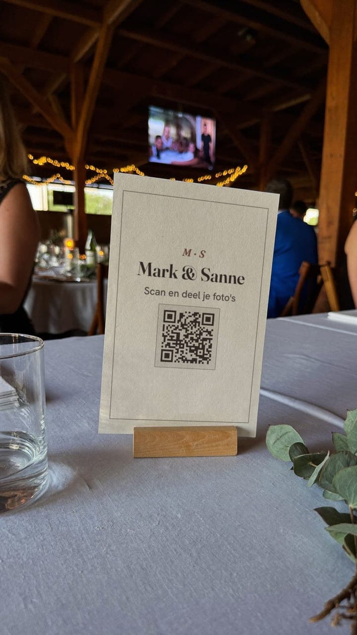Het QR-tafelkaartje van Mark & Sanne op een gedekte tafel, met het grote scherm op de achtergrond